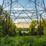 Power lines cross through a park and over the Connecticut River and attach to a tower on the other side.