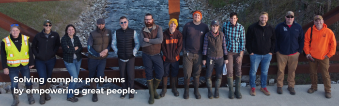 Drone photo of EnviroScience Ecological Restoration Services team standing on a bridge over a stream, wearing field gear and safety vests, showcasing teamwork and fieldwork culture.