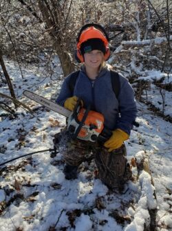 EnviroScience field biologist in winter protective gear preparing a chainsaw for invasive vegetation control during a snowy field project.