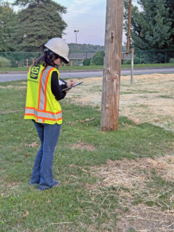 An EnviroScience inspector wearing a hard hat and safety vest takes notes on a clipboard while evaluating a site for environmental compliance.