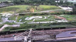 Aerial view of a restored meandering stream and wetland system surrounded by vegetation, with nearby rail lines and industrial infrastructure.