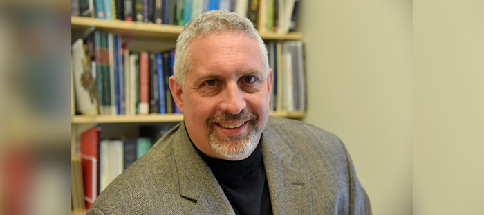 Portrait of Dr. Alan Christian smiling in front of a bookshelf, wearing a blazer and black turtleneck.