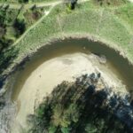 Aerial view of a restored river bend along the Chagrin River in the South Chagrin Reservation, Moreland Hills, Ohio. The image shows a curved channel with a sandy point bar on the inside of the bend and stabilized, vegetated banks along the outer edge. Surrounding areas include grassy floodplain, newly established vegetation, and adjacent park trails, illustrating bank stabilization, reduced erosion, and improved floodplain connectivity following restoration work.