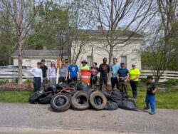 Group of volunteers standing behind bags of collected litter, tires, and debris after a community cleanup event.