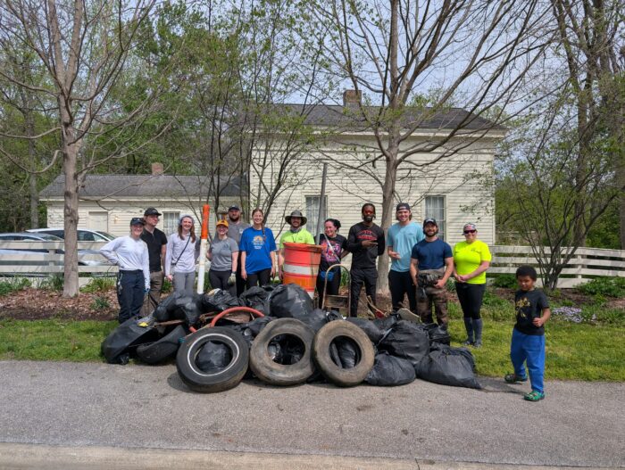 Group of volunteers standing behind bags of collected litter, tires, and debris after a community cleanup event.
